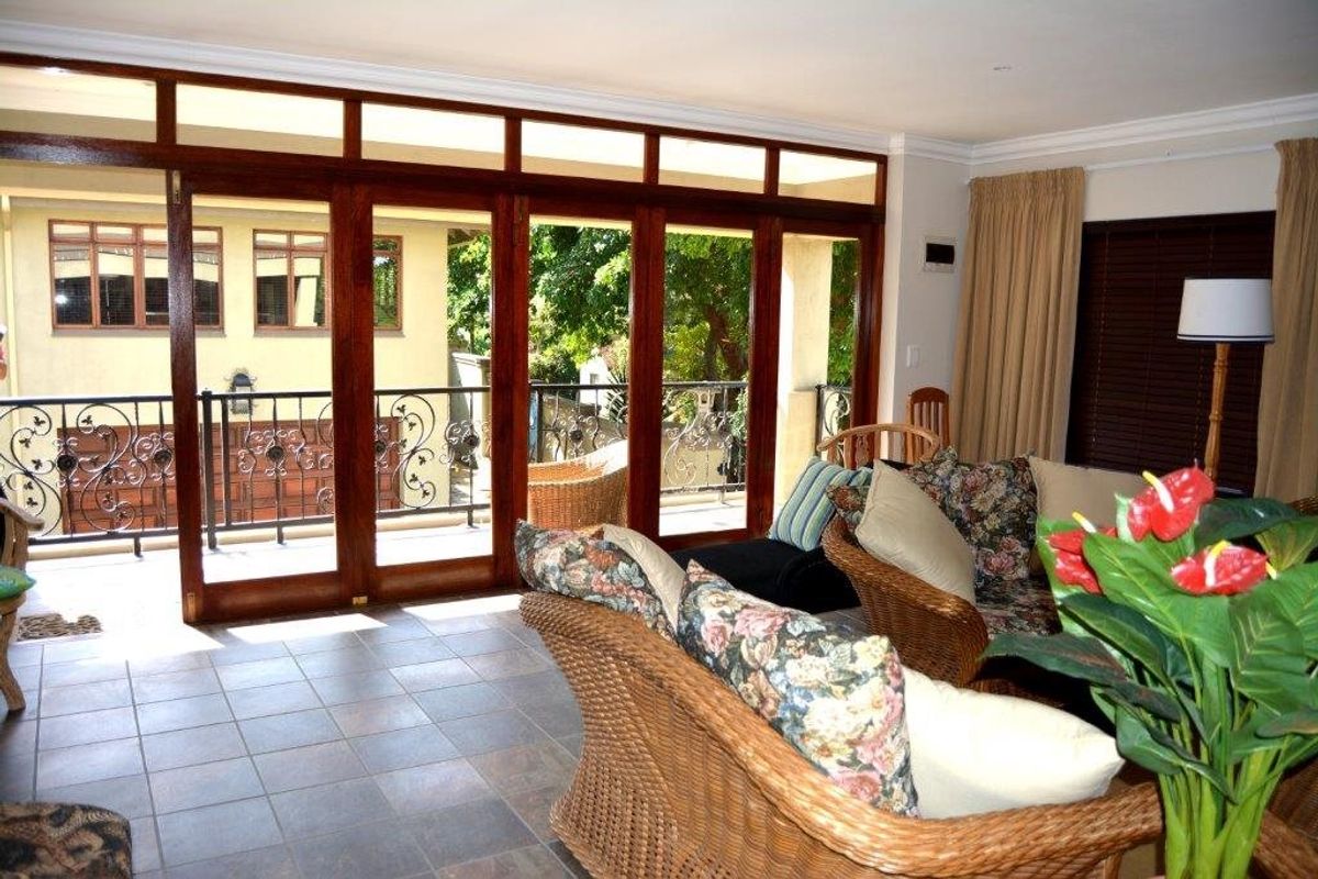 Spacious living area featuring large timber-framed sliding doors that open onto a balcony with wrought iron railings and garden views.