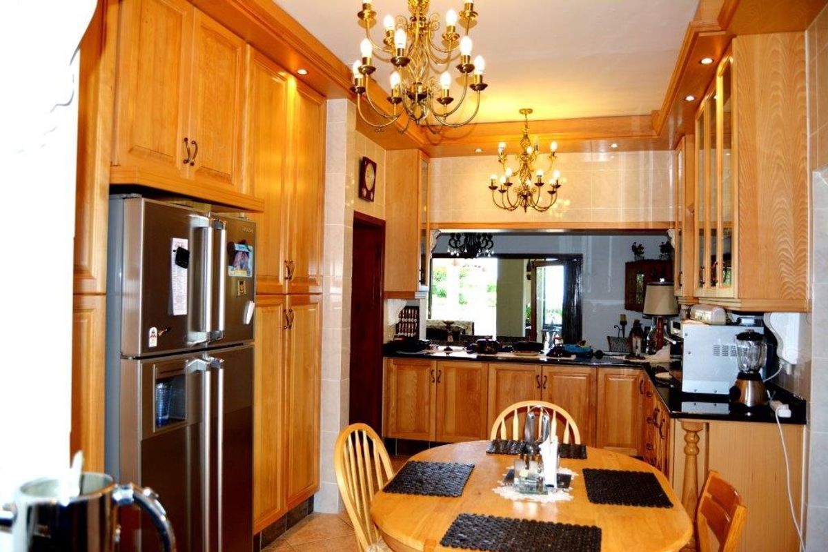 A traditional kitchen featuring extensive built-in wooden cabinetry, granite countertops, tiled backsplash, and dual chandeliers, offering a warm and functional cooking space.
