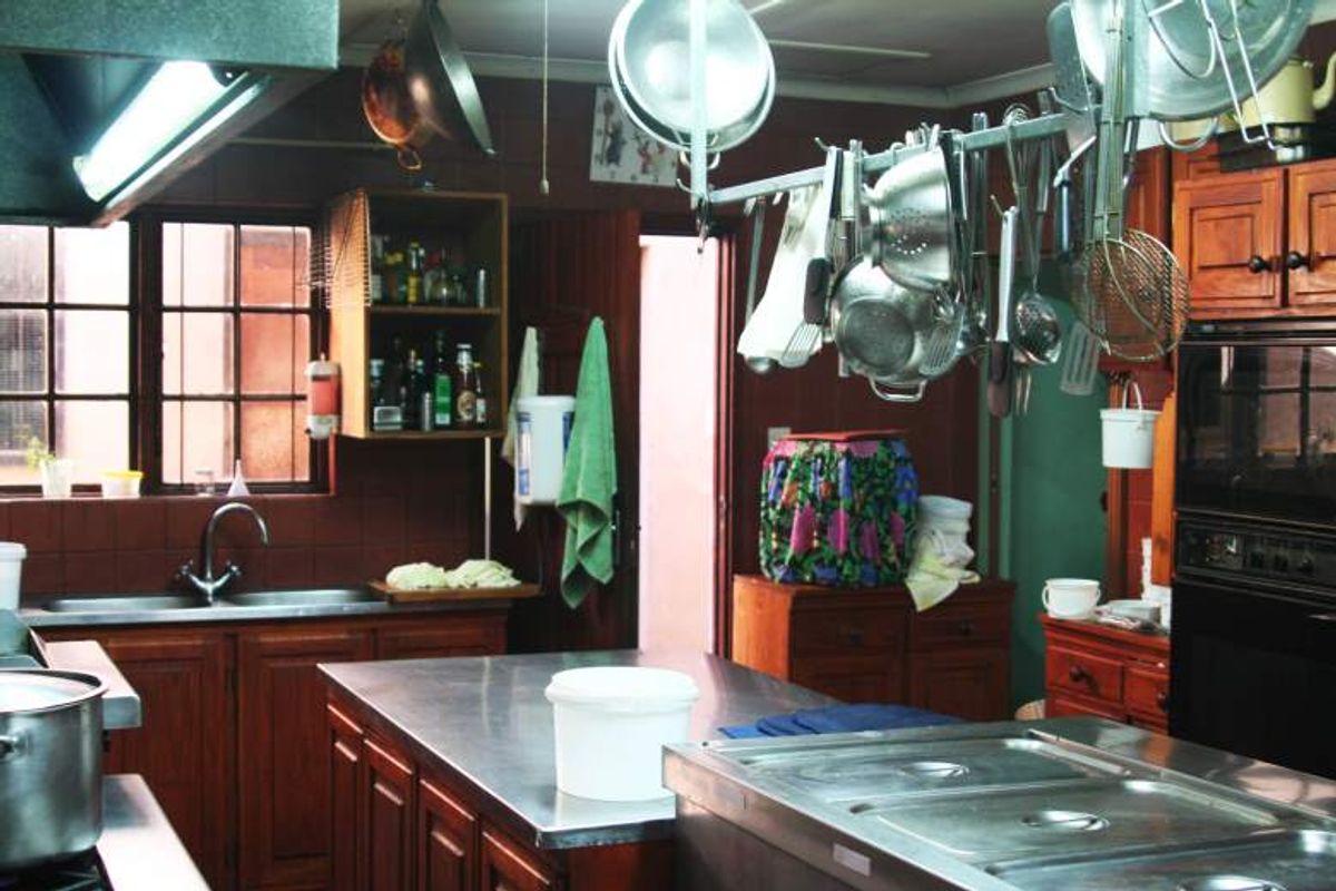 A commercial-style kitchen featuring stainless steel work surfaces, built-in wooden cabinetry, a double basin sink, and an overhead pot rack for efficient storage.