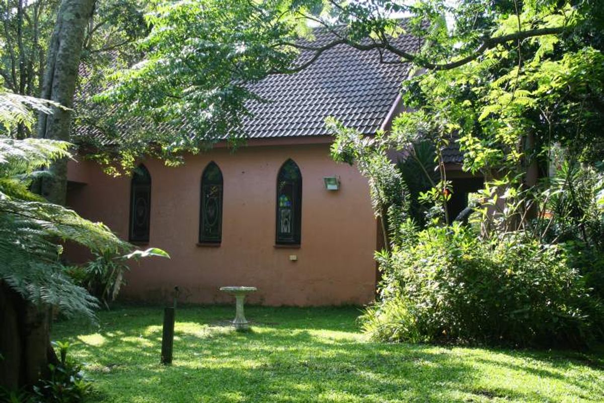 Rear view of a commercial building featuring a tiled roof and distinctive pointed arch stained glass windows set within a landscaped garden area.