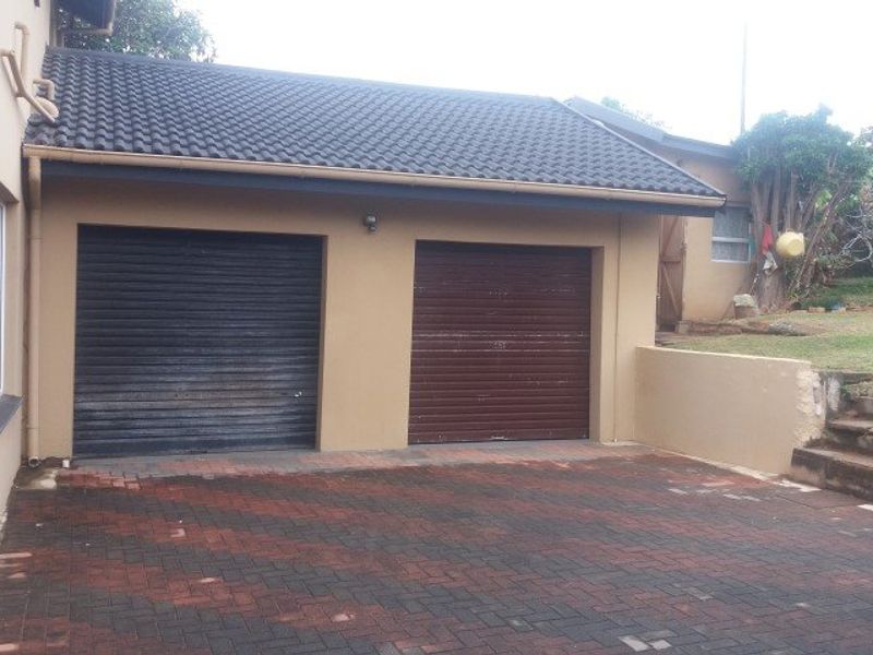 A double garage with roller doors and a paved driveway, featuring a tiled roof and adjacent retaining wall with steps leading to the garden.