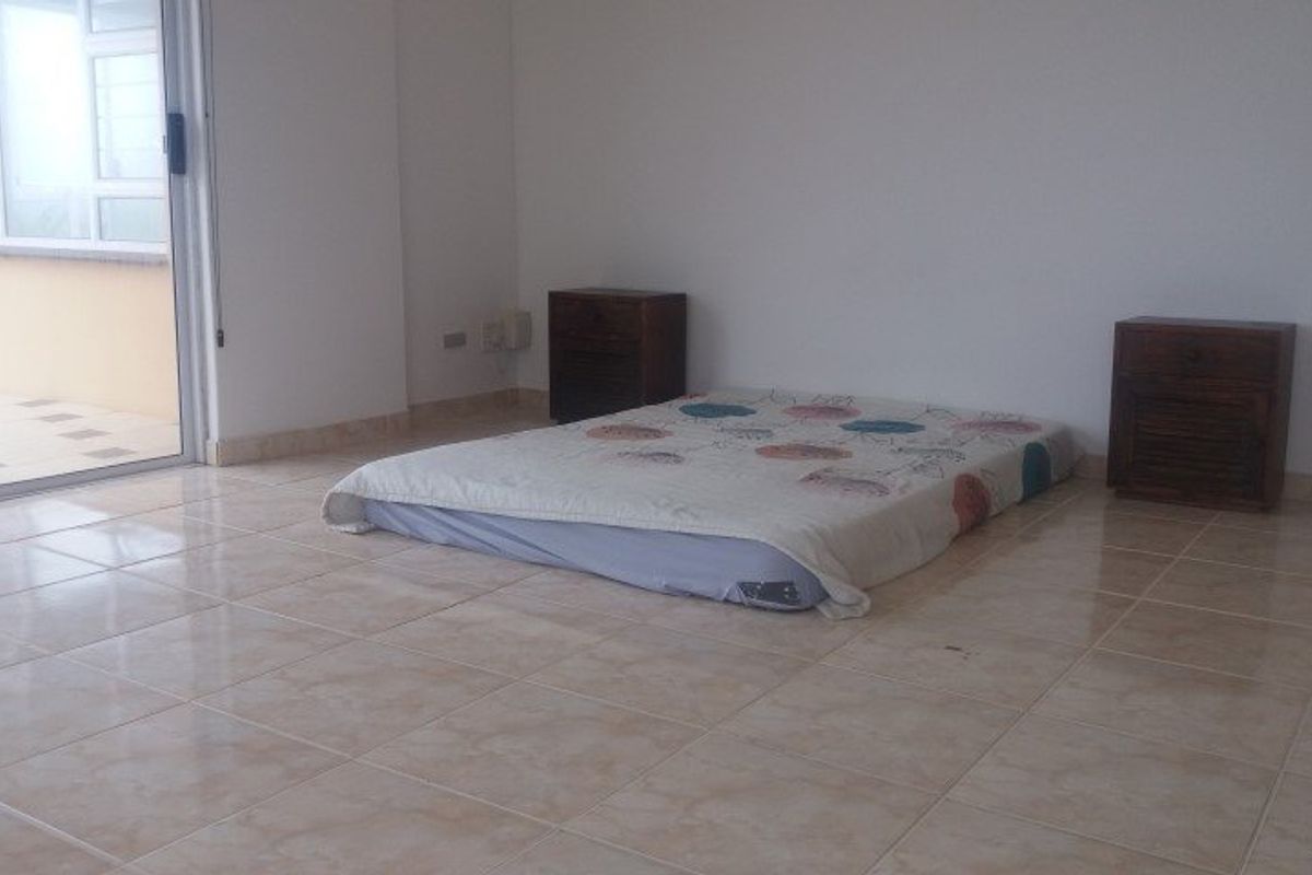 A spacious bedroom featuring neutral tiled flooring and a sliding glass door providing access to an outdoor area.