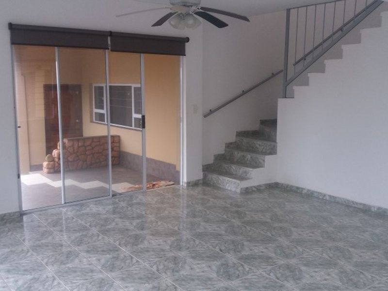 An open-plan living area featuring tiled flooring, a staircase with a metal handrail, a ceiling fan, and sliding glass doors leading to an outdoor space.