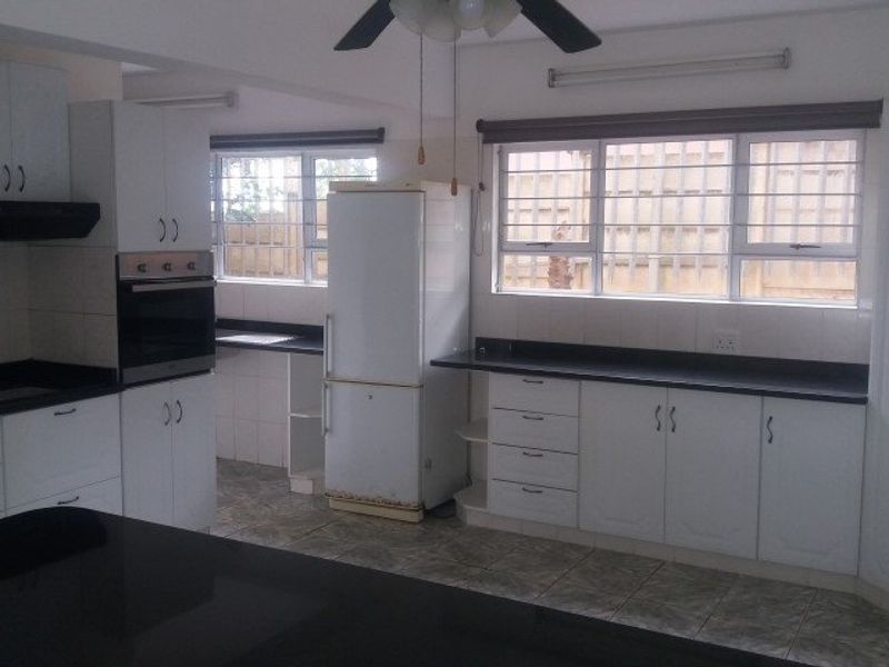 A functional kitchen featuring white built-in cabinetry, dark countertops, tiled flooring, and security bars on the windows.