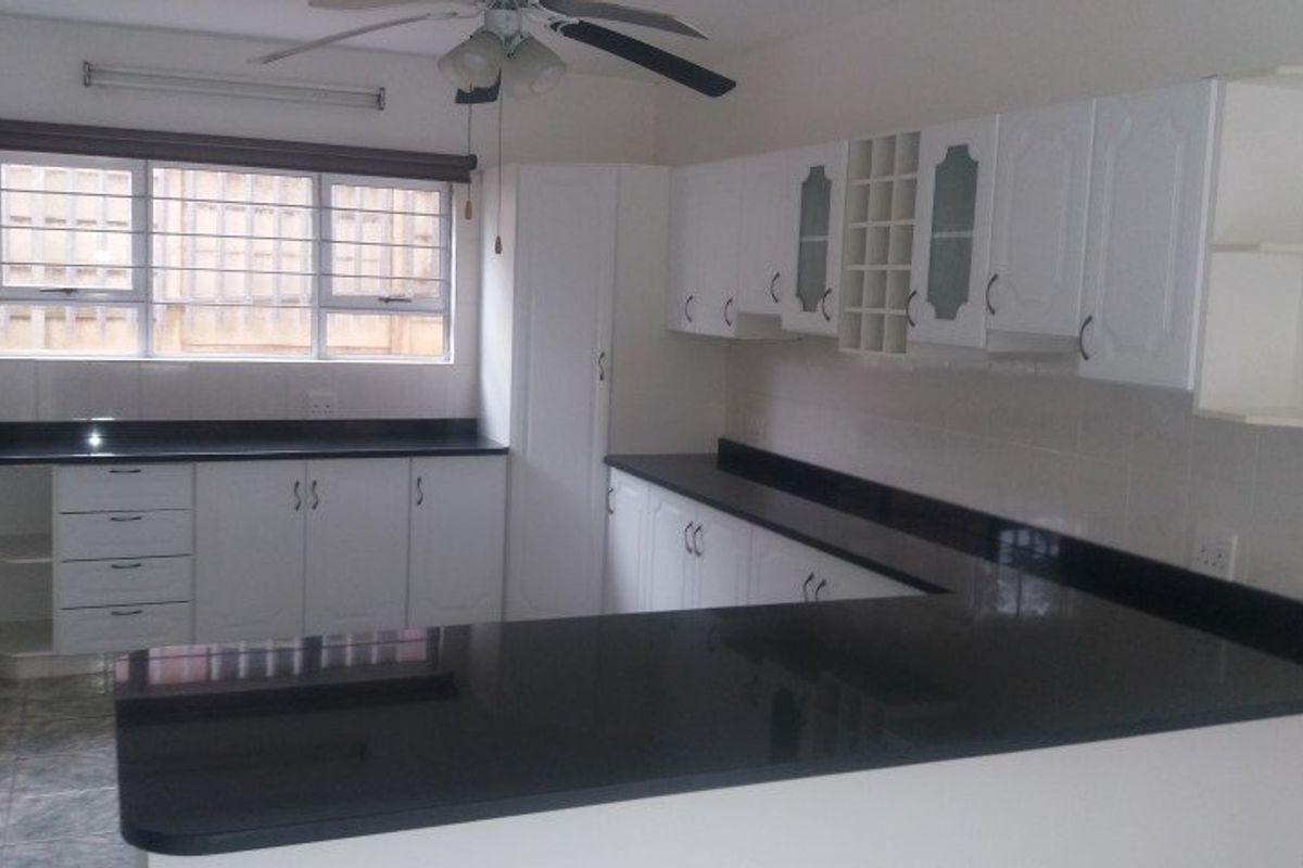 A clean, functional kitchen featuring white cabinetry, contrasting black granite countertops, and tiled flooring, offering a bright and well-maintained workspace.