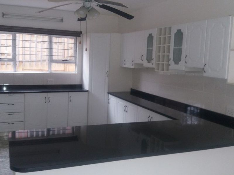 A clean, functional kitchen featuring white cabinetry, contrasting black granite countertops, and tiled flooring, offering a bright and well-maintained workspace.