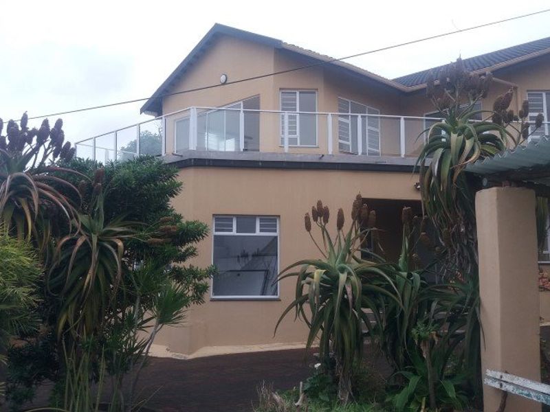 A two-story residential property featuring a prominent upper-level balcony with glass balustrades, aluminium window frames, and a paved driveway area.