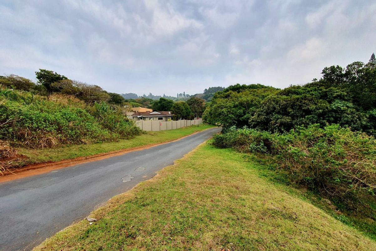 A view of the asphalt access road and surrounding natural vegetation leading towards the residential property boundary.