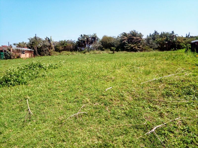 A view of a vacant residential plot featuring open grassy terrain and established perimeter vegetation.