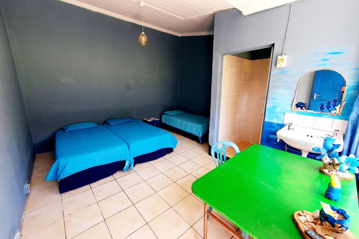 A basic bedroom featuring tiled flooring, a small en-suite shower area, and a wall-mounted basin, suitable for budget commercial accommodation.