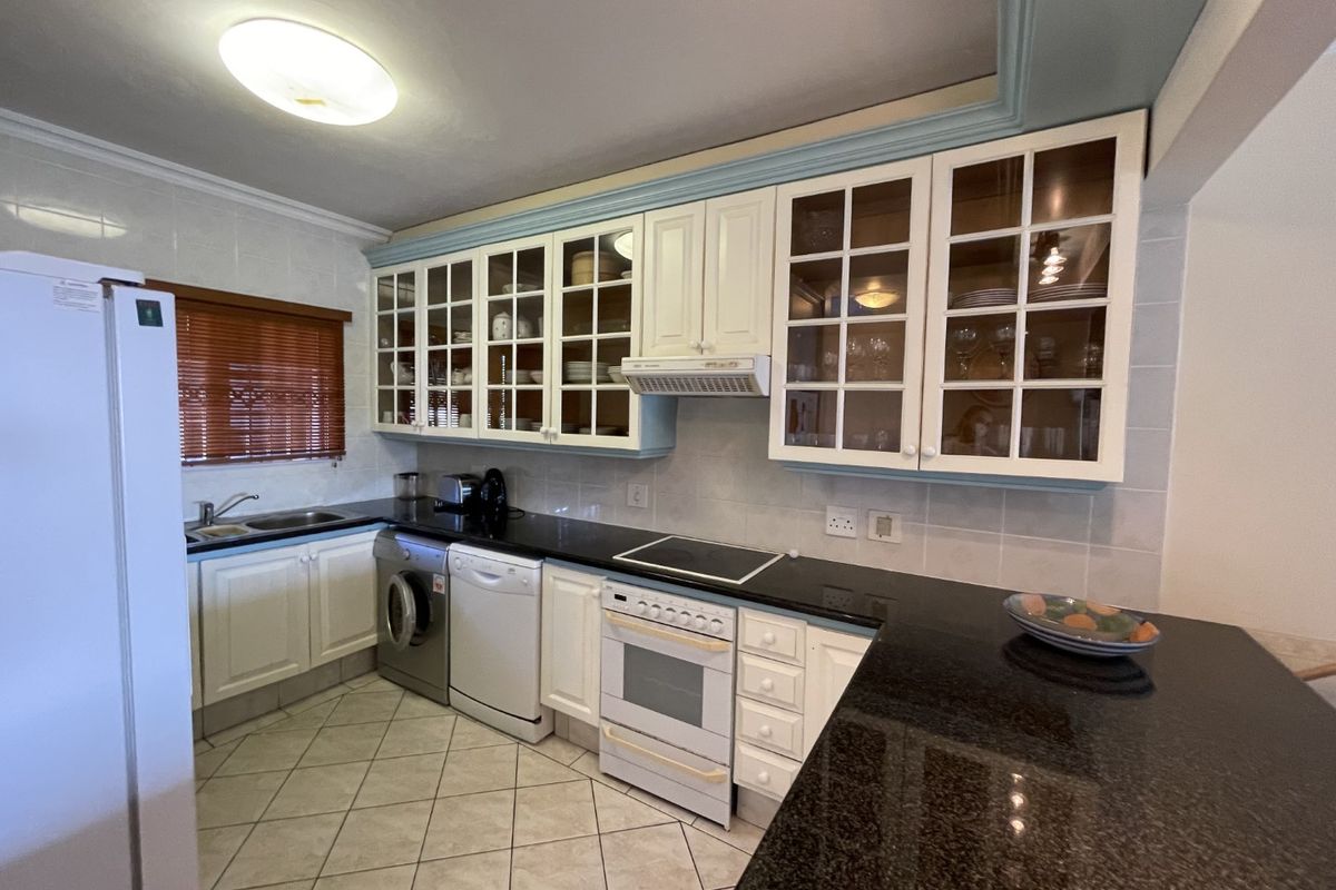 A functional kitchen featuring granite countertops, glass-front cabinetry, built-in oven with hob, and tiled finishes throughout.