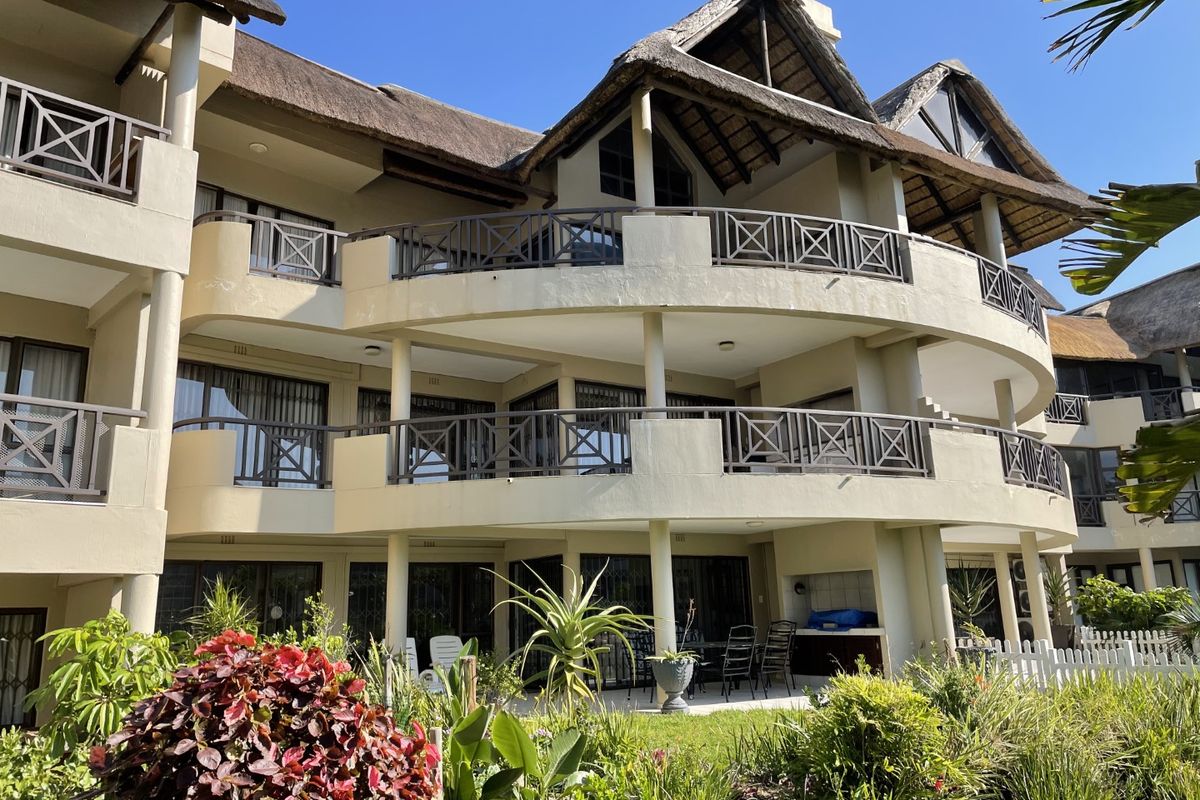 Rear elevation of a multi-story apartment complex featuring thatched roofing, curved balconies with railings, and a ground-floor patio with a built-in braai area.