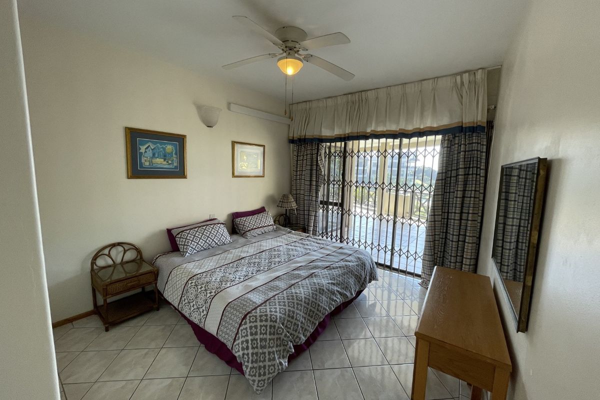 A bedroom featuring tiled flooring, a ceiling fan, and a sliding glass door with a security gate leading to an outdoor area.
