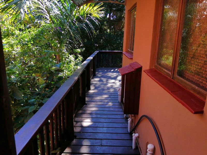 A wooden balcony deck featuring a timber balustrade, overlooking lush garden greenery, attached to the side of the townhouse.