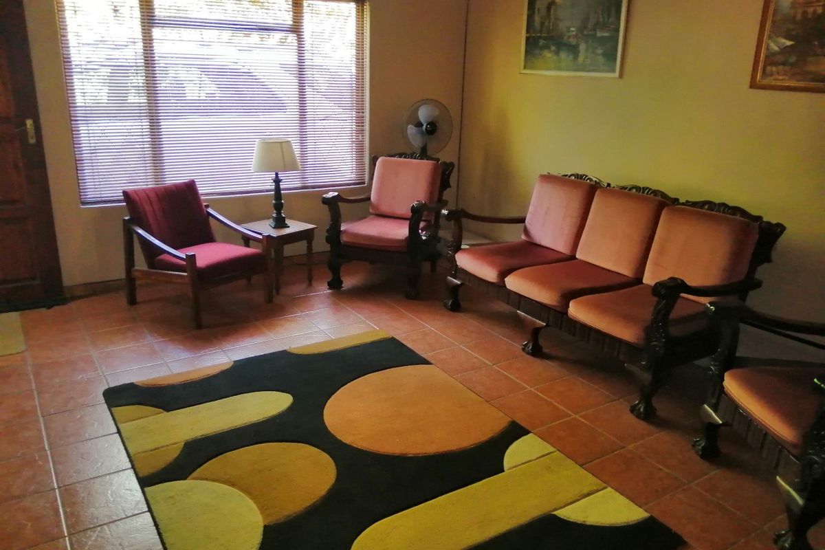 A living room featuring terracotta-style floor tiles and a large window with venetian blinds, offering a traditional layout.