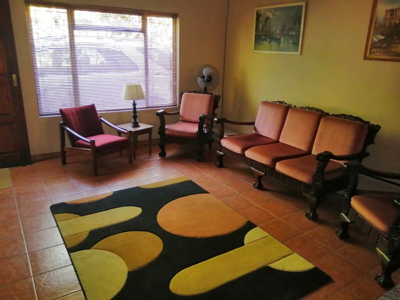 A living room featuring terracotta-style floor tiles and a large window with venetian blinds, offering a traditional layout.