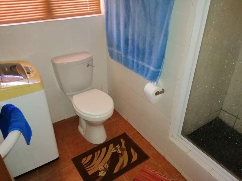 A functional bathroom featuring a toilet, shower enclosure, and tiled finishes, with natural light provided by a window with venetian blinds.
