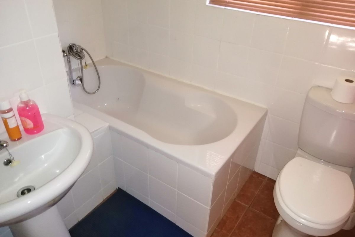 A compact bathroom featuring a built-in bathtub, pedestal basin, and toilet with tiled finishes, requiring some cosmetic updates to improve its overall condition.