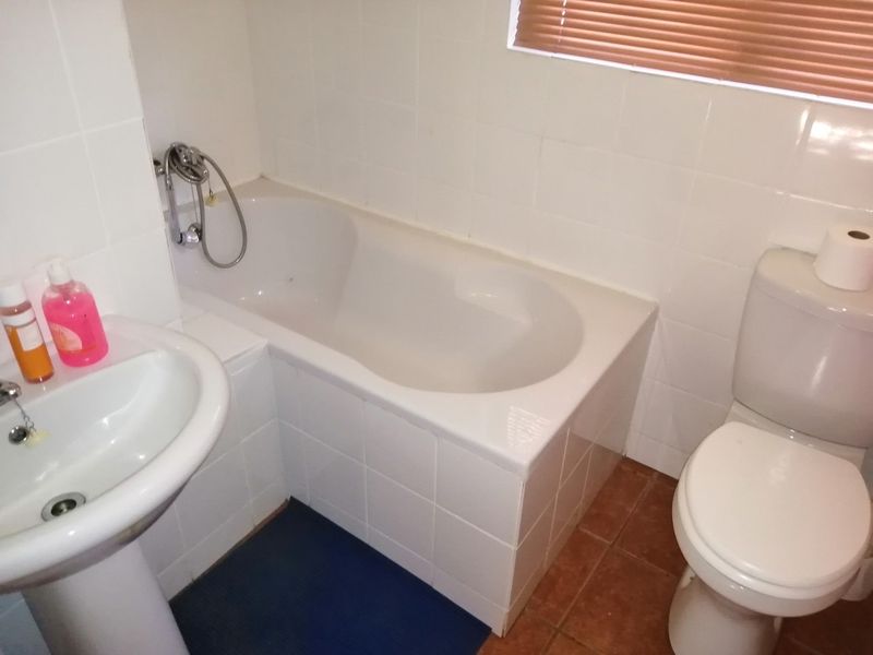 A compact bathroom featuring a built-in bathtub, pedestal basin, and toilet with tiled finishes, requiring some cosmetic updates to improve its overall condition.