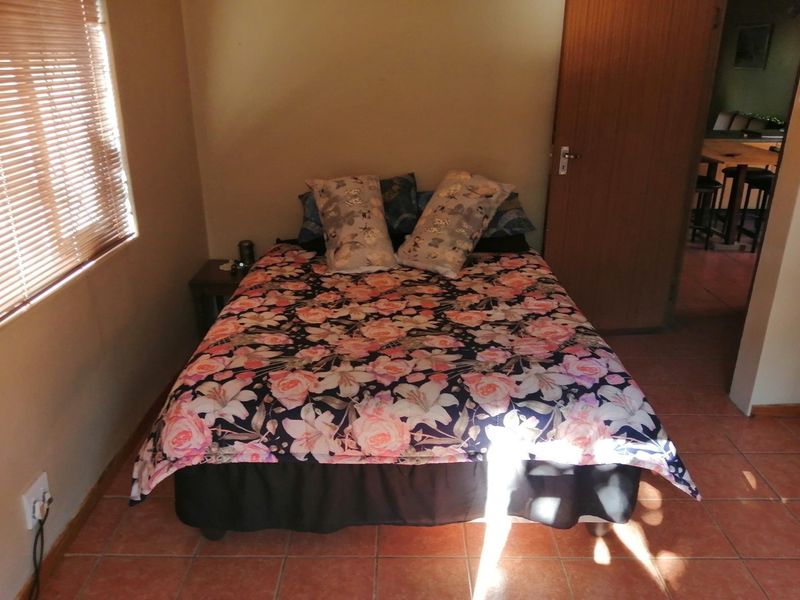 A functional bedroom featuring tiled flooring, a timber door, and venetian blinds, offering a simple and practical living space.