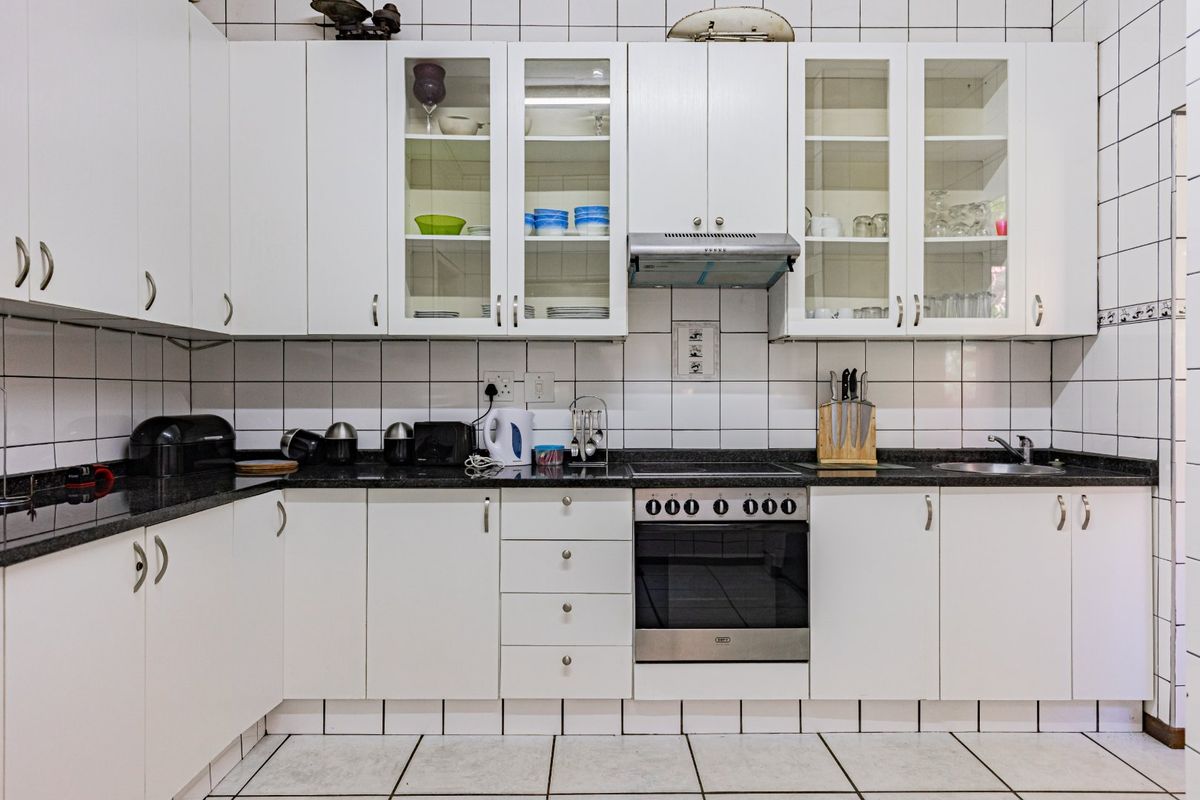 A functional kitchen featuring white cabinetry, granite countertops, built-in oven, extractor fan, and classic white tiled walls and flooring.