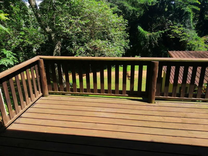 An elevated timber balcony deck featuring a wooden balustrade, overlooking a lush green garden area.