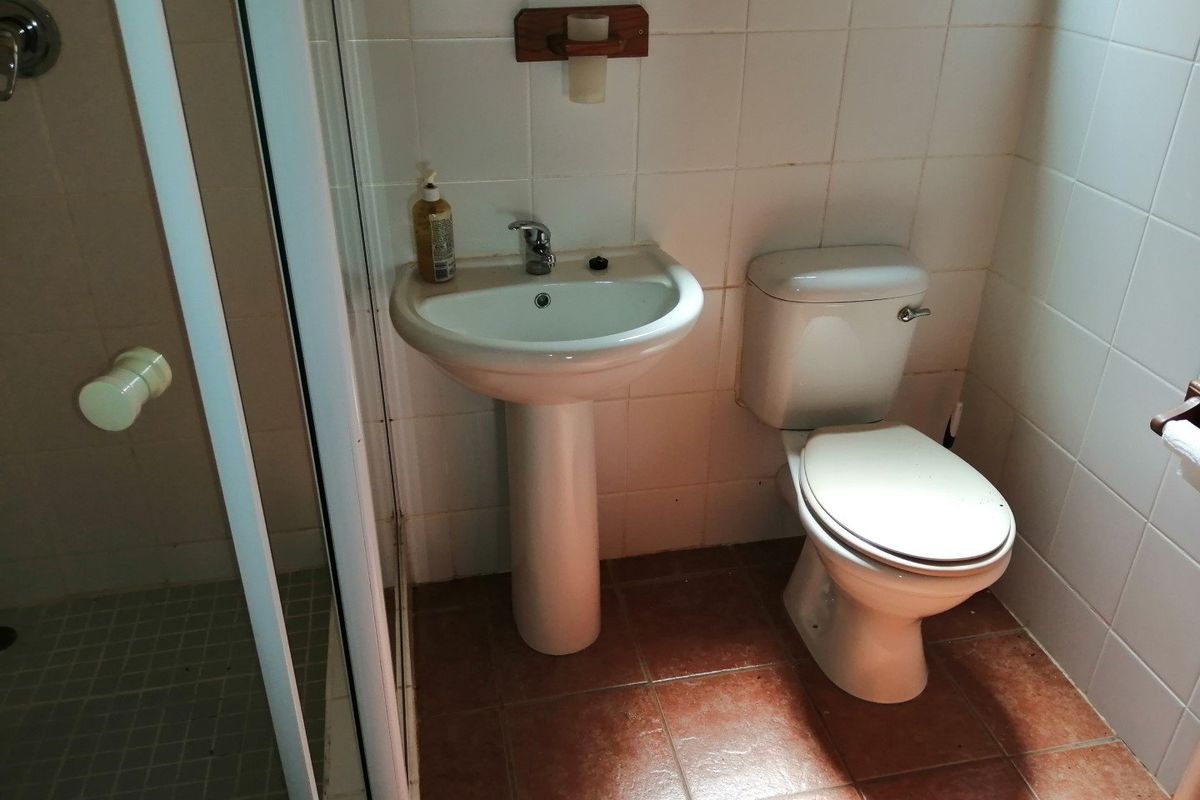 A functional bathroom featuring a pedestal washbasin, toilet, and shower enclosure with tiled walls and flooring, requiring cosmetic updates to modernize the space.
