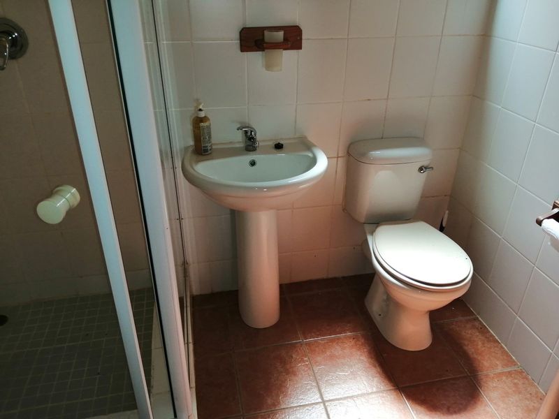 A functional bathroom featuring a pedestal washbasin, toilet, and shower enclosure with tiled walls and flooring, requiring cosmetic updates to modernize the space.