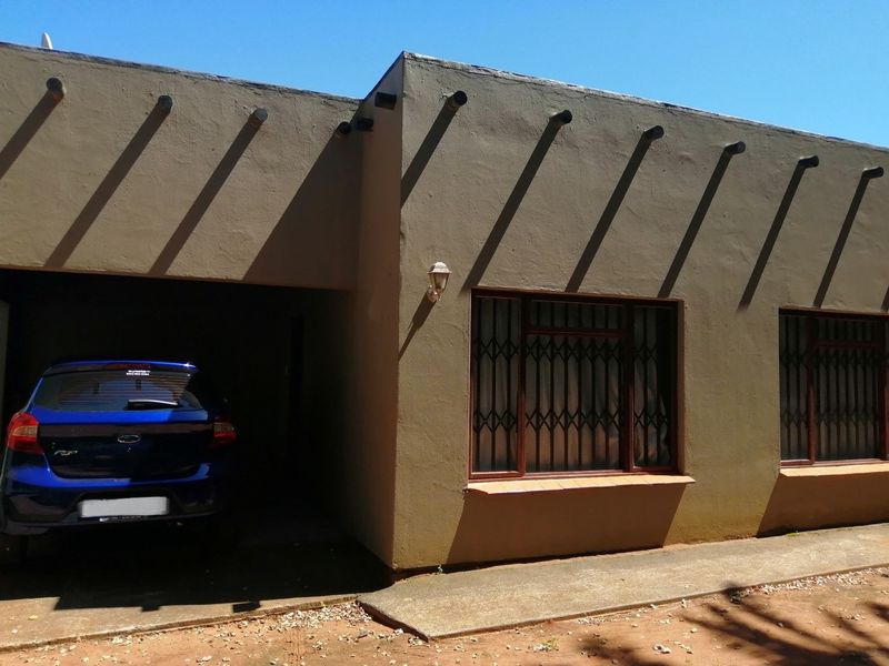 Front elevation of a townhouse featuring a carport, security gates on windows, and exposed rafter details.