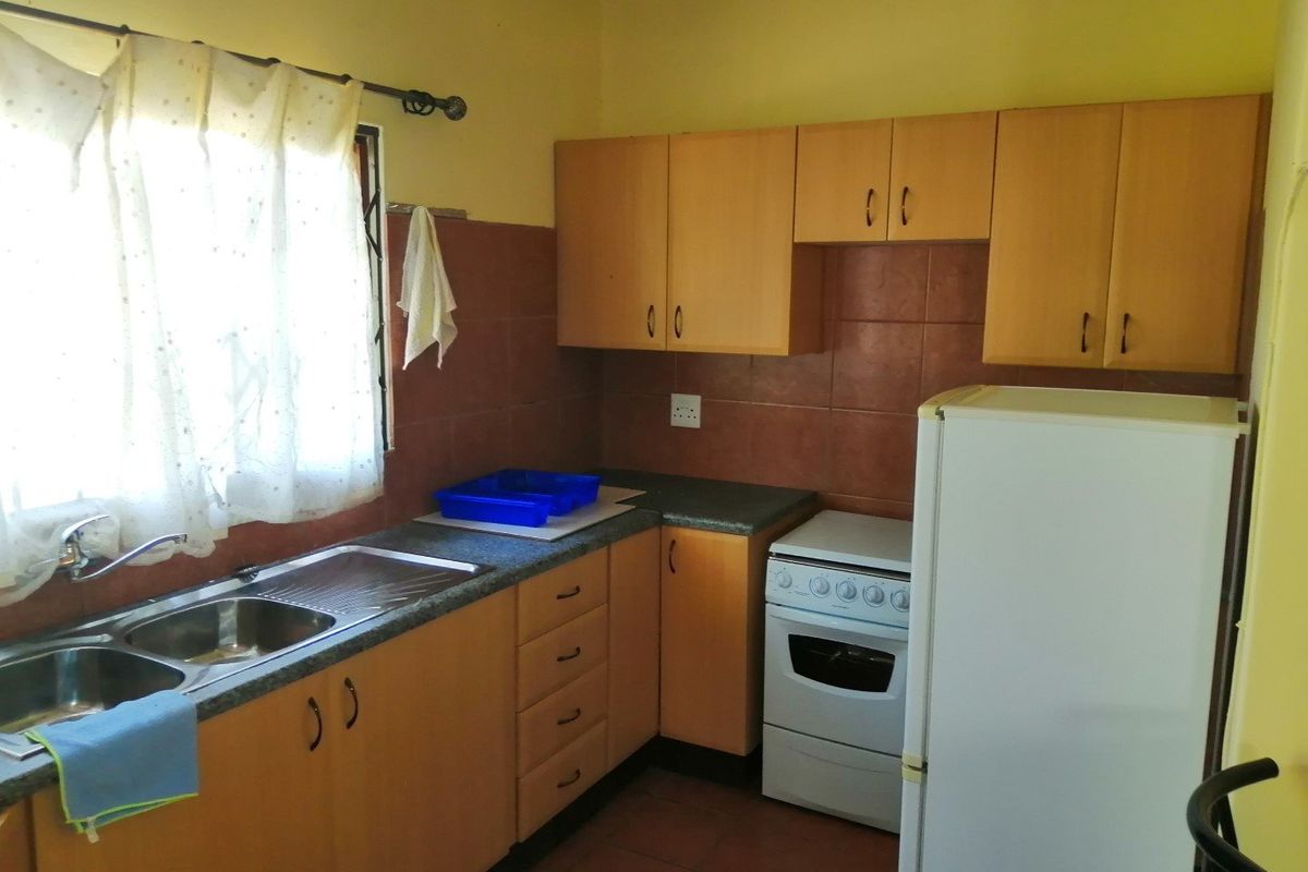 A functional kitchen featuring laminate cabinetry, a double bowl stainless steel sink, tiled splashbacks, and a freestanding stove.