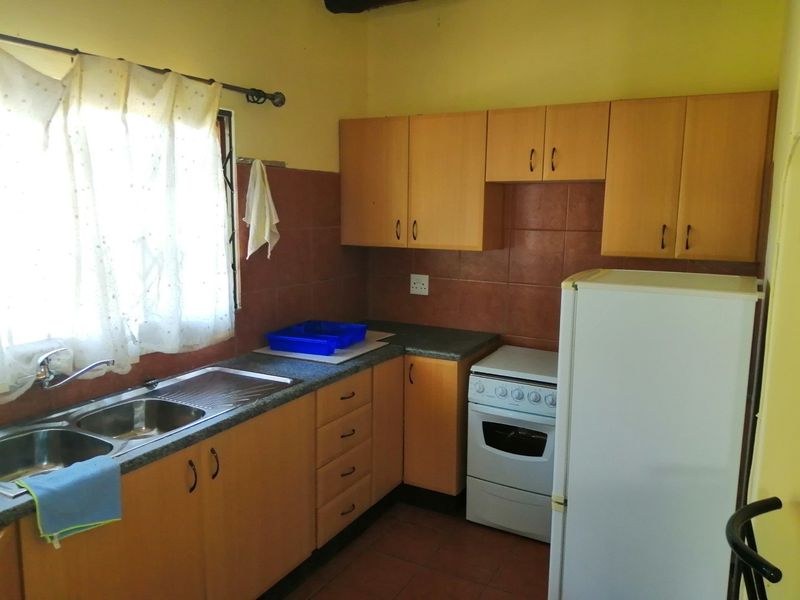 A functional kitchen featuring laminate cabinetry, a double bowl stainless steel sink, tiled splashbacks, and a freestanding stove.