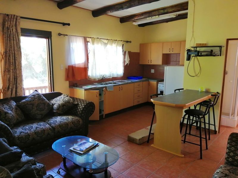 Open-plan living and kitchen area featuring exposed timber beams, tiled flooring, and a breakfast bar, offering a functional layout with potential for modernization.