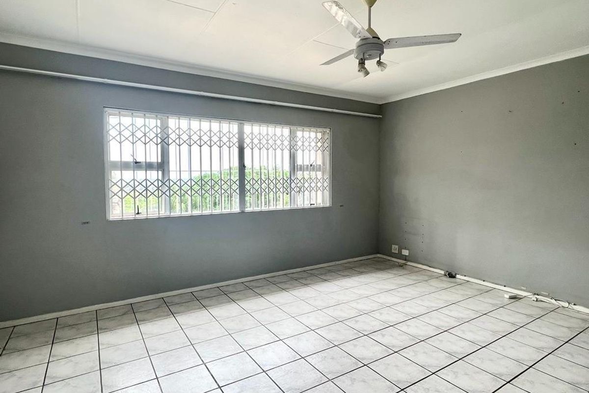 An empty bedroom featuring grey painted walls, white tiled flooring, a ceiling fan, and a window fitted with security bars.
