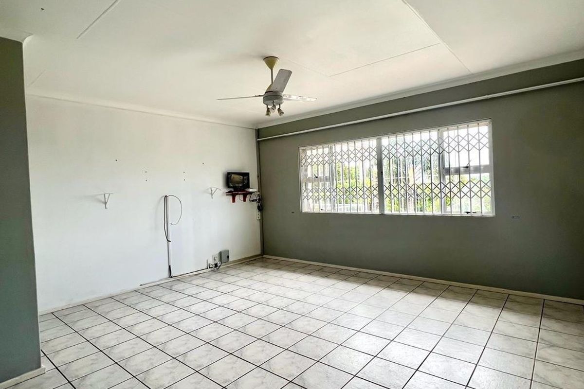 A spacious, empty living room featuring tiled flooring, a ceiling fan, and security bars on the windows.