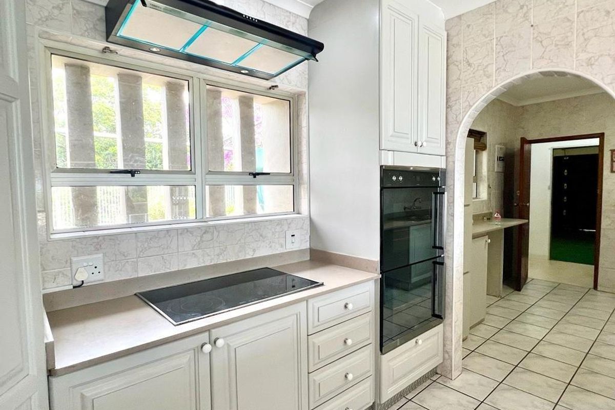 A functional kitchen featuring built-in cabinetry, a glass cooktop, extractor fan, and a double wall oven, with an arched entryway leading to a scullery area.
