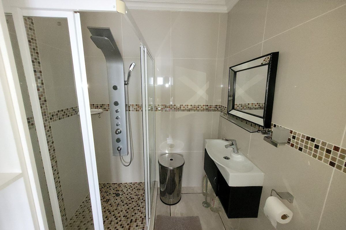 Modern bathroom featuring a glass shower enclosure with a multi-jet shower panel, wall-mounted vanity with basin, and neutral tiled finishes with mosaic accents.