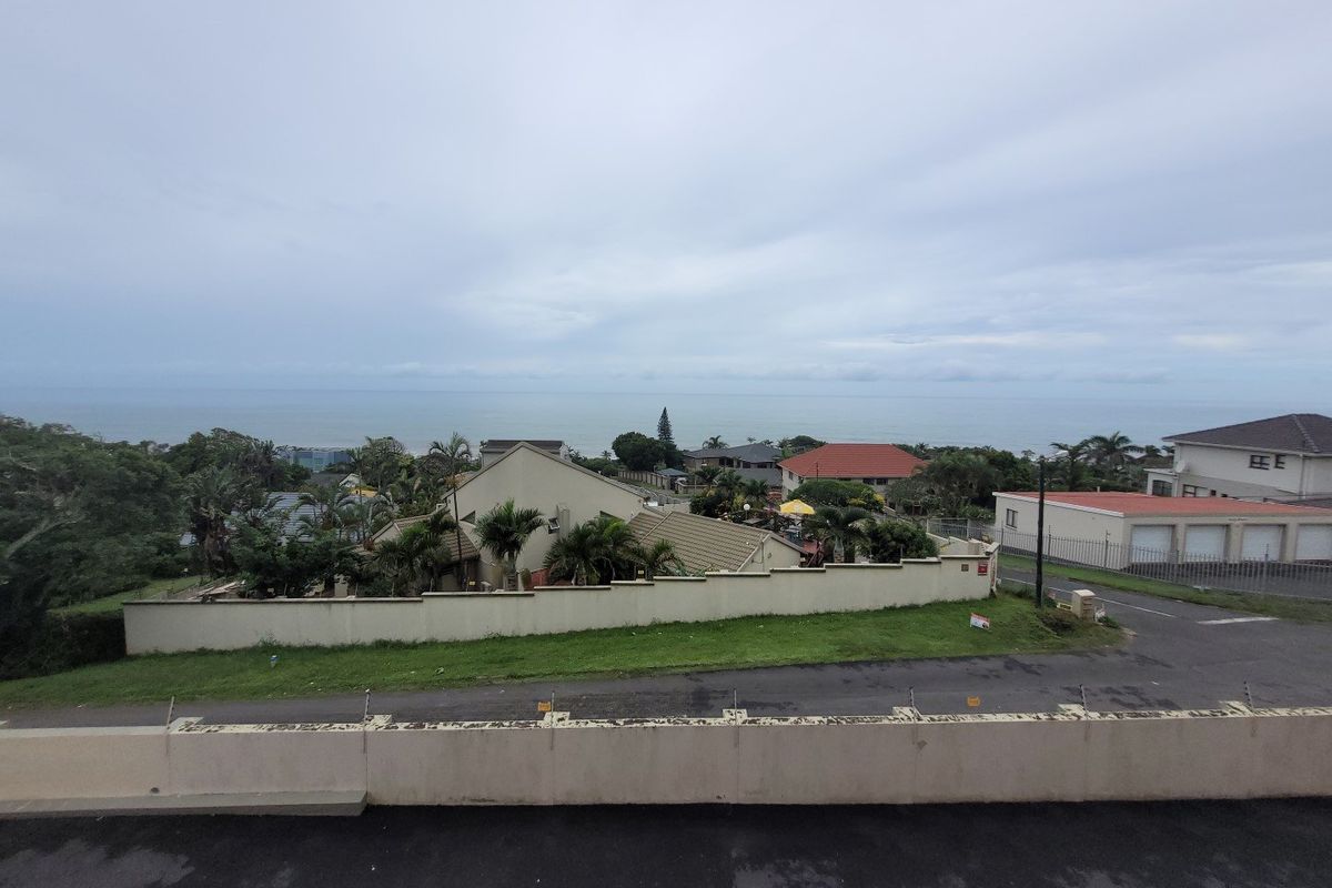 Elevated view overlooking the surrounding neighborhood and coastline, featuring a perimeter wall with security fencing in the foreground.