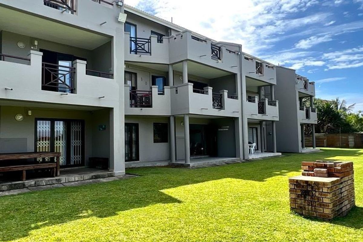 Rear view of the apartment complex featuring ground floor patios, upper-level balconies, and a communal garden area with a brick braai.