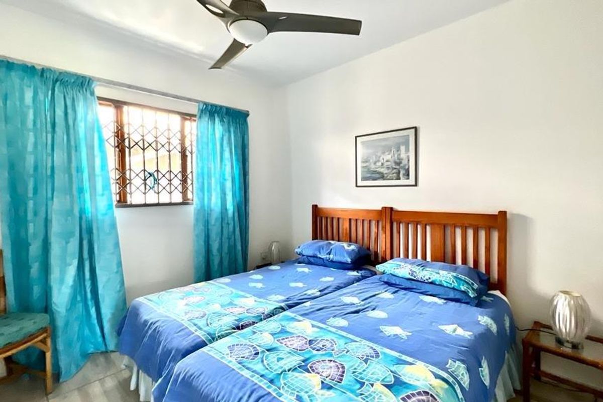 A functional bedroom featuring a ceiling fan and a window fitted with a security gate, providing natural light and ventilation.