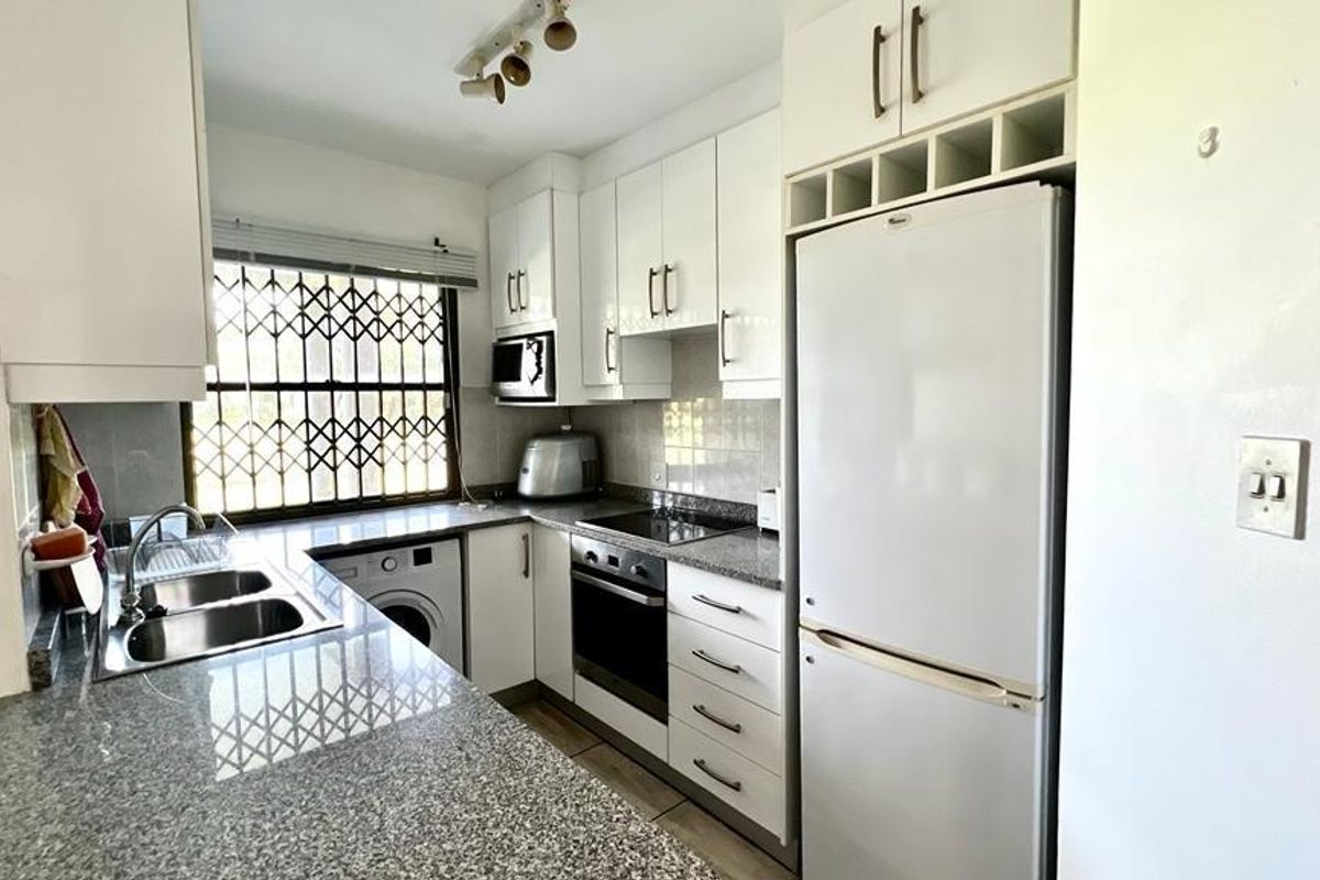 A functional kitchen featuring granite countertops, built-in cabinetry, an integrated oven and hob, and a double stainless steel sink with security window bars.