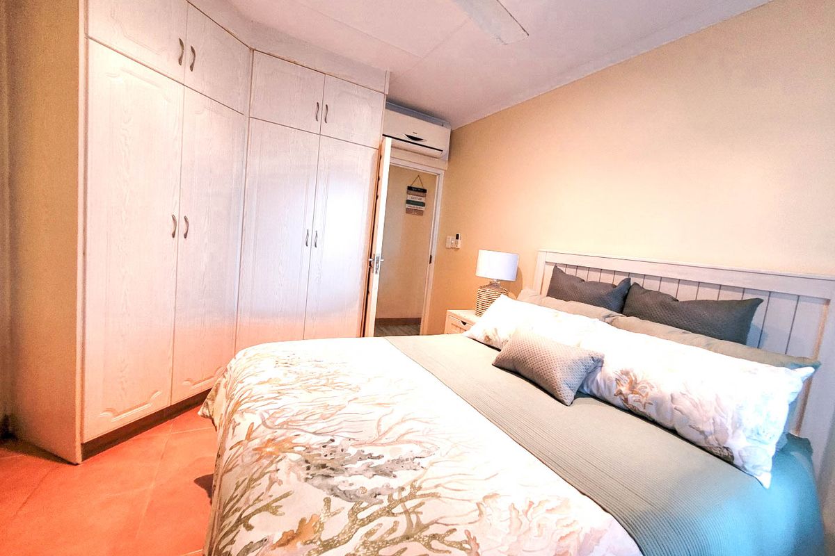 A bedroom featuring built-in cupboards, a ceiling fan, and a wall-mounted air conditioning unit with tiled flooring.