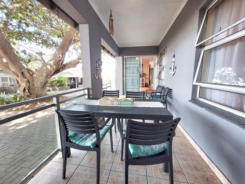 A covered patio area featuring tiled flooring, metal railings, and access to the interior through a security gate and windows.