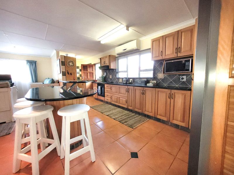 Open-plan kitchen featuring wooden cabinetry, granite countertops, built-in appliances, and a breakfast bar, seamlessly flowing into the adjacent living area.