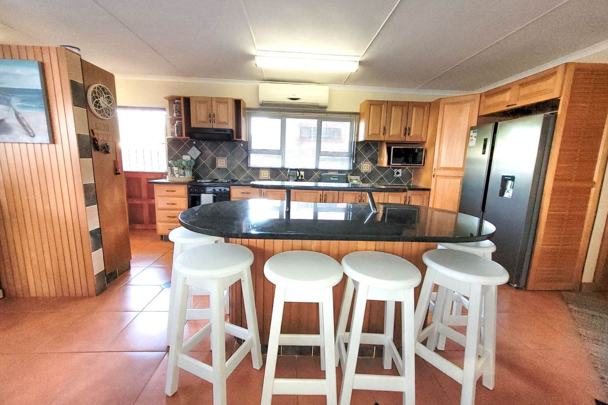 Spacious kitchen featuring wooden cabinetry, a large granite-topped island with breakfast bar seating, tiled flooring, and integrated appliances.