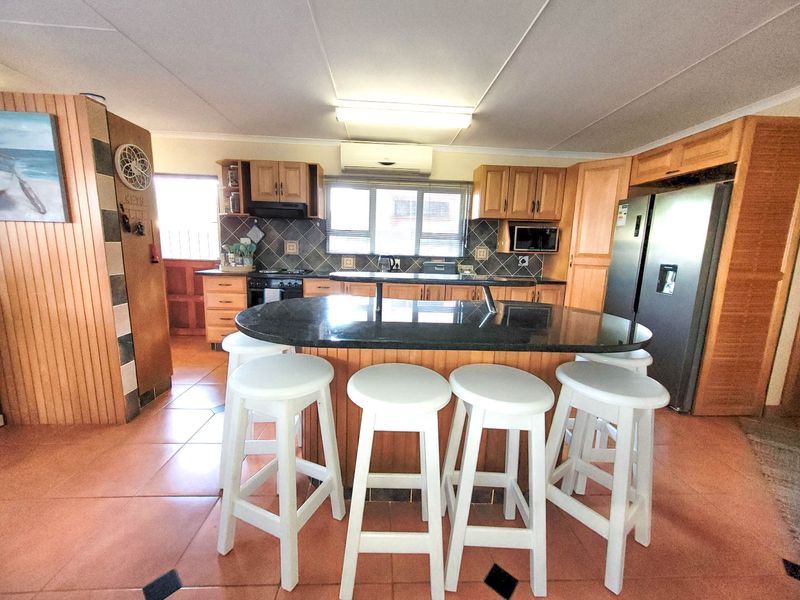 Spacious kitchen featuring wooden cabinetry, a large granite-topped island with breakfast bar seating, tiled flooring, and integrated appliances.