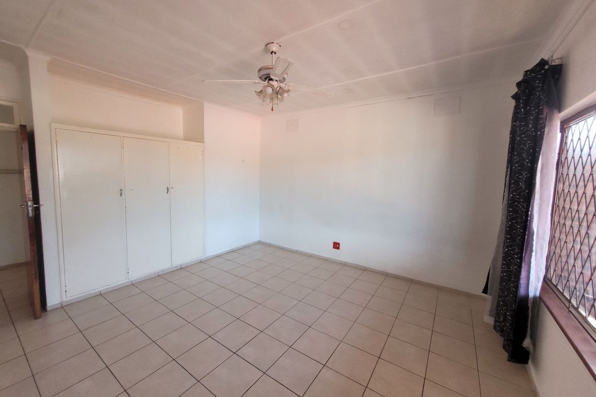 An empty bedroom featuring tiled flooring, built-in cupboards, and a ceiling fan, offering a blank canvas for personalization.
