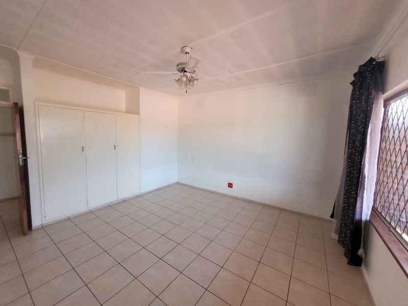 An empty bedroom featuring tiled flooring, built-in cupboards, and a ceiling fan, offering a blank canvas for personalization.