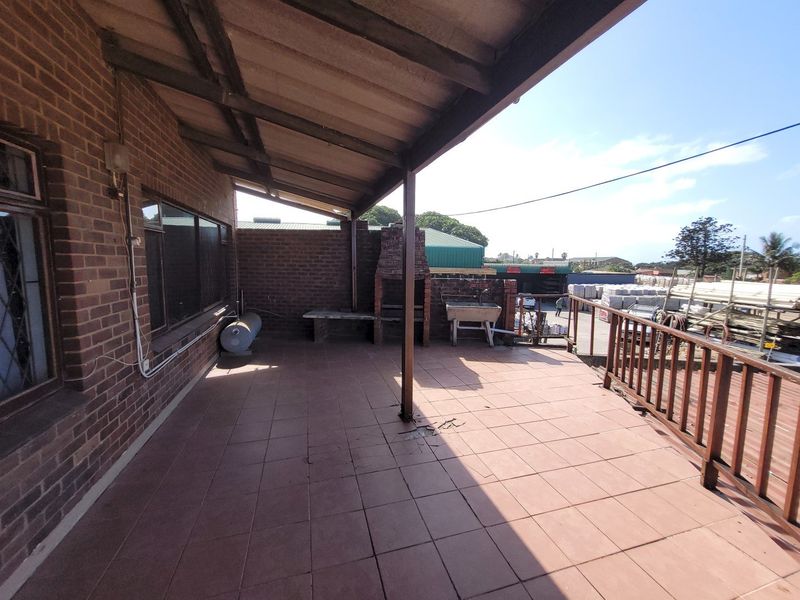 Covered outdoor patio featuring a built-in brick fireplace, concrete sink, and timber balustrade, offering a functional space for outdoor entertaining.