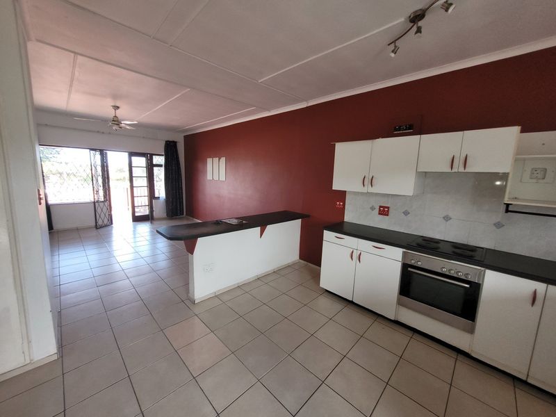 Open-plan living and kitchen area featuring tiled floors, built-in cabinetry with integrated oven and hob, and direct access to a balcony.