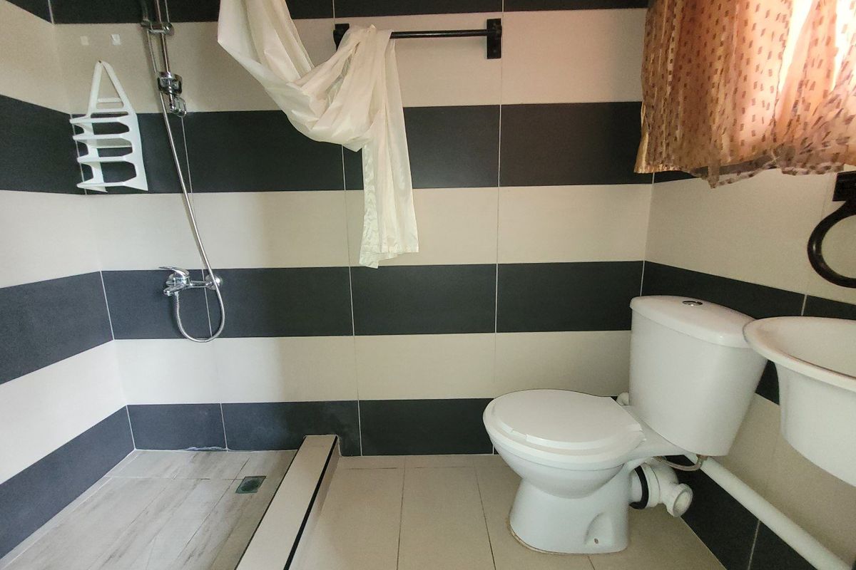 A compact bathroom featuring black and white horizontal wall tiles, a standard toilet, wall-mounted basin, and a shower area with exposed plumbing.